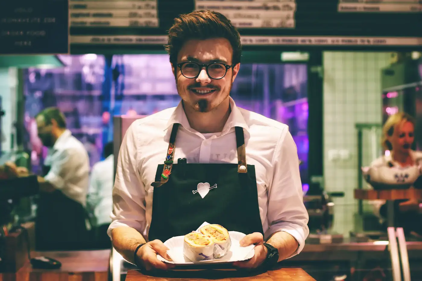 Garçom sorrindo com um prato na mão no salão de um restaurante