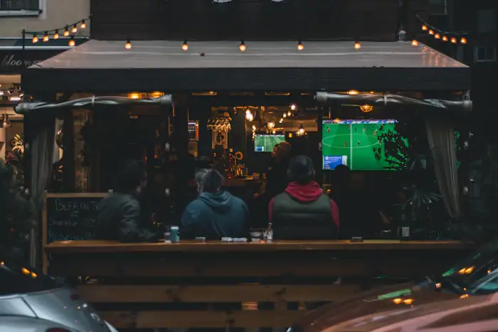Bar à noite com mesas cheias e futebol na TV