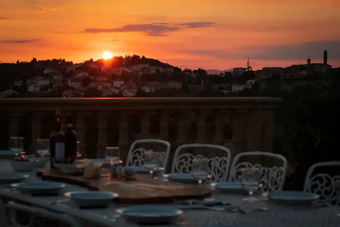 Mesas num terraço com o sol se pondo atrás dos morros da cidade