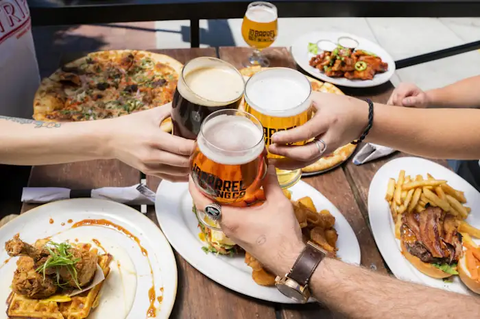 Amigos brindando com chopp numa mesa com pizza e porções